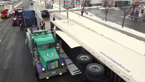 Semi-truck-trailer-fallen-on-side-with-emergency-vehicles-helping,-aerial-orbit-view