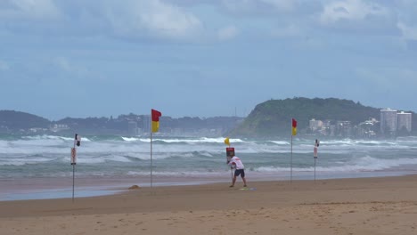 Strong-waves-crashing-onto-the-shore-with-lifeguard-setting-up-safety-sign-at-Broadbeach,-Gold-Coast,-Queensland,-Australia