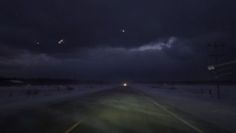 Toma-Pov-De-Un-Automóvil-Conduciendo-Por-Una-Carretera-Con-Ventisca-Invernal-Y-Nieve-En-La-Carretera-Por-La-Noche,-Ontario,-Canadá