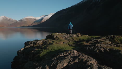 Excursionista-Caminando-A-Través-Del-Afloramiento-Del-Lago-Reflectante-Con-Revelaciones-De-Montañas-Nevadas-En-Wasdale-Lake-District-Reino-Unido