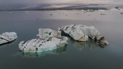 Ascending-aerial-shot-view-of-Swimming-icebergs-and-ice-flow-at-Jokulsarlon-Glacier-during-cloudy-day-in-Iceland