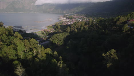 Aerial-shot-in-Bali-flying-over-blue-lake-ata-Mt-Batur-surrounded-by-fishertown-and-a-forests-on-a-mountain