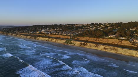 Aerial-view-rising-up-from-waves,-in-front-of-a-luxury-neighborhood,-golden-hour-in-San-Diego,-California,-USA