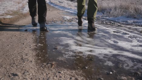 Two-people-hiking-on-a-winter-path-through-snowy-moorland,-walking-over-solid-frozen-ice-and-hard-packed-dirt