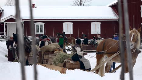 Horse-driven-sledges-with-people-dressed-in-old-contemporary-cloths-have-just-arrived-at-courtyard-with-an-old-red-house-in-the-background