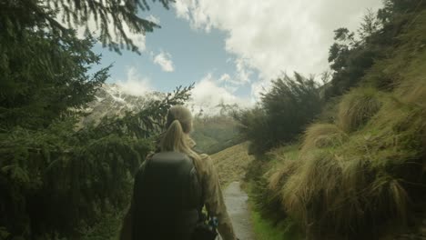 Mujer-Mochilera-Rubia-Caminando-A-Través-De-La-Vegetación-Nativa-Revelando-Impresionantes-Montañas