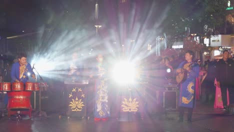 Una-Banda-Vietnamita-Tradicional-Vestida-De-Azul-Actúa-De-Noche-En-La-Ciudad-De-Ho-Chi-Minh-En-Vietnam,-Con-Un-Miembro-Tocando-La-Batería-Y-Otro-Tocando-Un-Instrumento-De-Cuerda