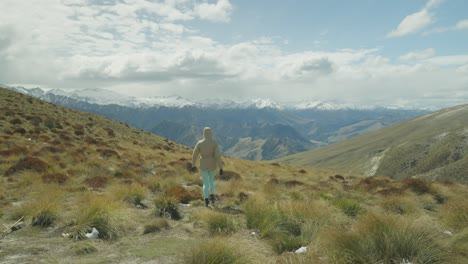 Woman-walking-through-alpine-tussock-field-high-in-mountains,-New-Zealand