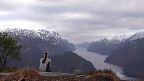 Young-woman-hiking-in-Norway-sits-at-overlook,-enjoys-view-of-Veafjord-in-Vestland