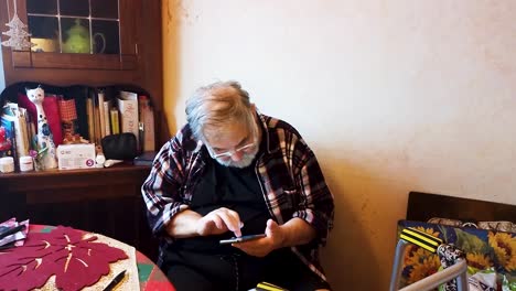 Senior-elderly-70s-man-user-holding-smartphone-watching-mobile-video-calling-online-looking-at-screen-relaxing-on-kitchen-chair-at-home,-older-grandparent-learn-using-modern-technology