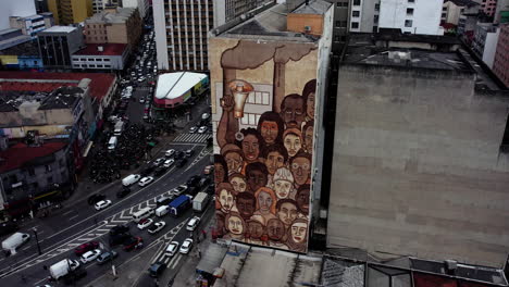 Aerial-view-in-front-of-the-“Workers-of-Brumadinho”-mural-in-downtown-Sao-Paulo,-sunny-Brazil---decending,-tilt,-drone-shot