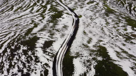 Aerial:-Following-a-white-car-on-muddy-dirt-road,-partially-covered-with-snow