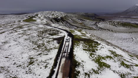 Aerial:-Following-a-car-driving-on-a-mountain-road-partially-covered-with-snow