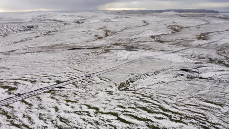 Aerial:-Panoramic-drone-shot-of-one-car-driving-in-the-hills-partially-covered-with-snow