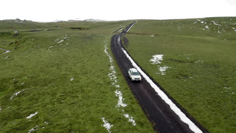 Aerial-front-view:-One-car-driving-on-a-muddy-mountain-road-partially-covered-with-snow
