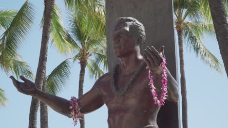 Vista-Del-Torso-De-La-Estatua-De-Duake-Paoa-Kahanamoku-En-Un-Día-Soleado-Y-Ventoso-Con-Palmeras-En-El-Fondo-En-La-Playa-De-Waikiki-En-Hawaii