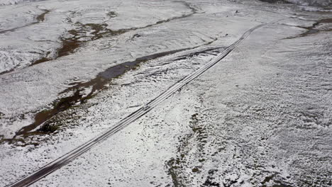 Aerial:-Following-a-white-car-on-muddy-dirt-road,-partially-covered-with-snow-in-Iceland-highlands