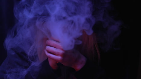 Person-with-a-black-hood-smoking-electronic-cigarette-while-stressfully-shaking-in-a-dark-room