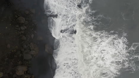 Luftaufnahme:-Von-Oben-Nach-Unten-Gerichtete-Umlaufbahnaufnahme-Von-Schäumenden-Wellen,-Die-Am-Schwarzen-Sandstrand-Von-Reynishjara-In-Island-Zerbrechen