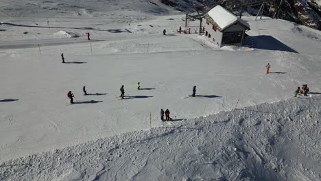 Vista-Aérea-De-Los-Esquiadores-Que-Van-Cuesta-Abajo-En-Una-Estación-De-Esquí-De-Los-Alpes-Suizos,-Tarifa-De-Saas
