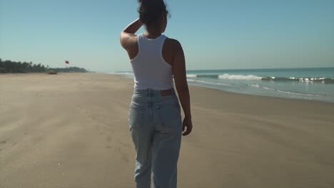 Mujer-Caminando-Por-La-Playa-Con-Jeans-Y-Una-Camisa,-Mirando-Al-Horizonte