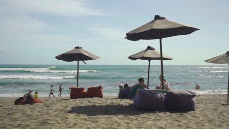 Entspannen-Sie-Sich-Unter-Einem-Sonnenschirm,-Entspannen-Sie-Sich-Auf-Sitzsäcken-Und-Beobachten-Sie-Surfer-Am-Strand-Von-Batu-Bolong-In-Bali-Canggu