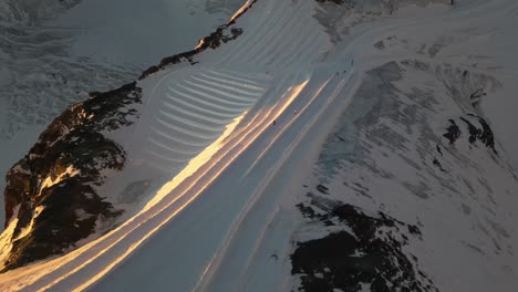 Antena,-Pistas-De-Esquí-Durante-Un-Amanecer,-Glaciar-Y-Rocas-En-Los-Alpes,-Montaña-Nevada