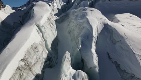 Aerial-tilt-up:-snow-covered-icy-peaks-in-a-glacier,-Switzerland,-alps