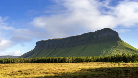 Time-lapse-of-rural-farming-landscape-with-grass-field-and-distant-coniferous-forest-with-moving-clouds-at-Benbulben-mountain-on-sunny-day-in-county-Sligo-in-Ireland