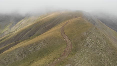 Drone-video-into-the-clouds-gravel-dirt-road-hills-foggy-mountain-Gramos-peaks
