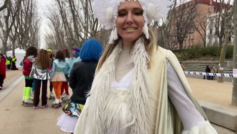Close-up-of-a-pretty-blonde-artist-girl-dressed-as-a-white-fairy-showing-her-costume-smiling-at-the-camera