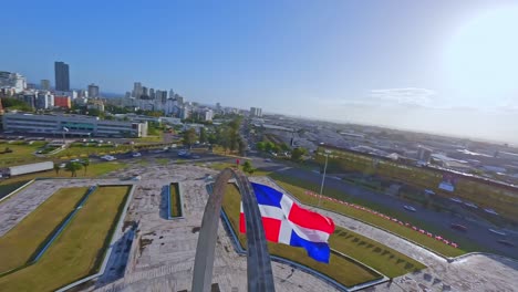Fpv-flight-over-city-of-Santo-Domingo-during-beautiful-sunny-day-at-Plaza-de-la-Bandera---Traffic-on-roundabout-in-capital
