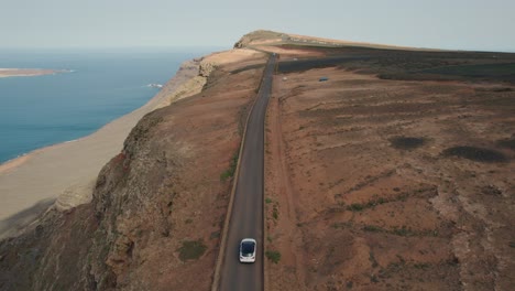 White-car-driving-on-a-costal-road-on-a-cliff-of-La-Graciosa-in-Spain-with-backdrop-of-the-Atlantic-Ocean