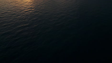 Luftaufnahme-über-Dem-Meer-Bei-Sonnenuntergang,-Stadt-Mit-Klippe-Im-Hintergrund-An-Bewölktem-Und-Goldenem-Tag