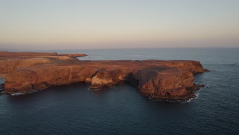 -Rocky-cliffs-of-Papagayo-island-looking-red-at-sunset-as-waves-gently-crush-against-them