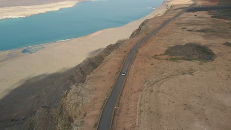Car-moving-on-a-road-on-a-cliff-of-Lanzarote-with-view-of-La-Graciosa-island-and-the-ocean