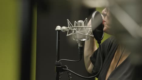 Woman-passionately-singing-into-mic-in-recording-studio-while-gesturing-hand,-slow-motion
