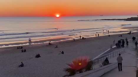 Silhouetten-Von-Menschen,-Die-Am-Sandstrand-Spazieren-Gehen,-Und-Surfer-Im-Hintergrund-Des-Sonnenuntergangs-An-Der-Atlantikküste-Portugals