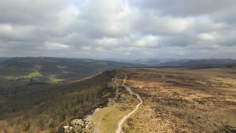Cinematic-aerial-footage-of-a-long-trail-through-open-moorland-and-steep-rock-formations