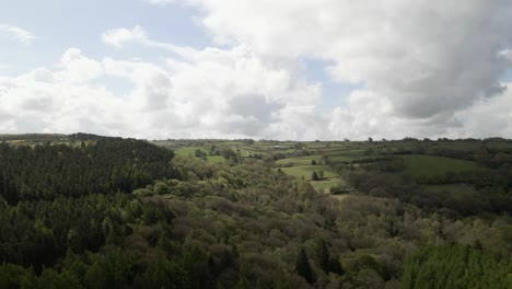 Aerial-drone-footage-flying-over-dense-green-forests-and-rolling-hills-with-fluffy,-white-clouds-in-the-sky