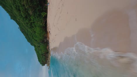 Vertical-FPV-drone-shot-cruising-over-beautiful-beach-to-the-green-forest-next-to-the-blue-sea