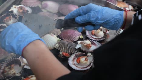 Chef-turning-with-his-hands-the-scallops-that-he-is-preparing-on-the-grill-in-a-typical-party