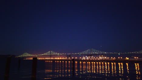 Gimbal-static-shot-of-the-Bay-Bridge-with-light-reflections-in-the-water-at-twilight-in-San-Francisco,-California