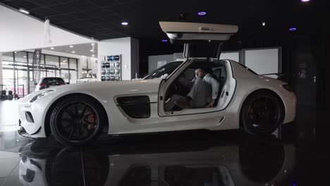 Slow-motion-shot-of-a-prestigious-man-leaving-a-white-Mercedes-Benz-AMG-GT-in-a-showroom