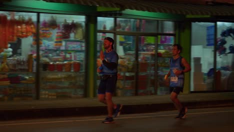 Two-athletes-running-the-Samui-Run,-being-cheered-and-applauded-by-supporters,-Koh-Samui-Island,-Thailand