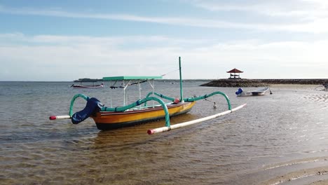Traditionelle-Holzboote-Kanu-Am-Strand-Von-Sanur,-Bali,-Indonesien,-Meer,-Blaues-Wasser,-Dock-Und-Pagodenpavillon-Im-Hintergrund,-Warmes,-Ruhiges,-Friedliches-Wetter-In-Südostasien