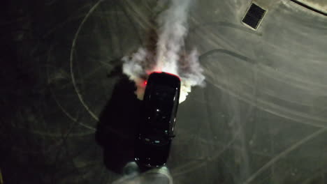 Aerial-view-above-a-car-drifting-at-a-parking-lot,-during-nighttime---top-down,-drone-shot