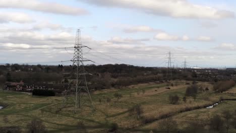 Aerial-view-Electricity-distribution-power-pylon-overlooking-British-parkland-countryside,-Wide-orbit