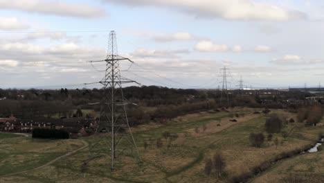 Electricity-distribution-power-pylon-overlooking-British-parkland-countryside,-aerial-view-pull-back-shot