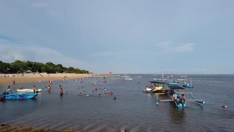Menschen-Schwimmen,-Gehen-Spazieren-Und-Boote-Segeln-Am-Strand-Von-Sanur-Mertasari,-Bali,-Indonesien,-Blaues-Wasser-Und-Weißer-Sand-Am-Warmen-Nachmittagshimmel,-Reisen-Und-Tourismus-Auf-Der-Insel-Der-Götter